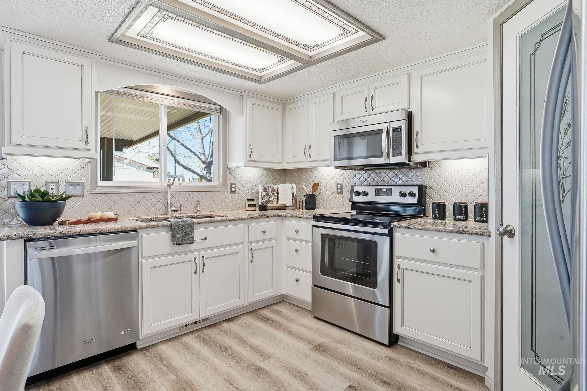 Kitchen featuring appliances with stainless steel finishes, light stone countertops, white cabinetry, light wood-style flooring, and a textured ceiling