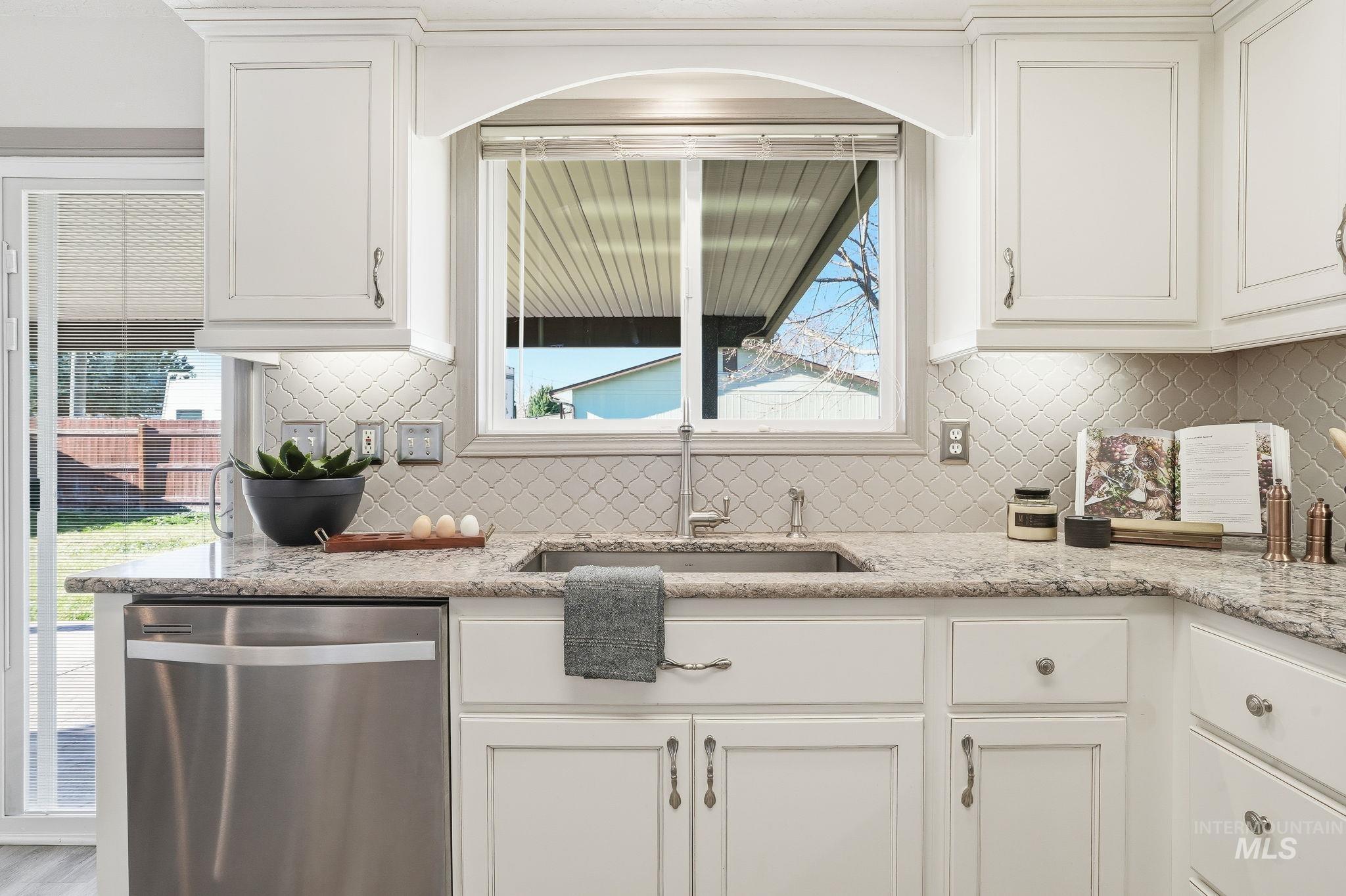 Kitchen with dishwasher, white cabinetry, light stone countertops, and backsplash
