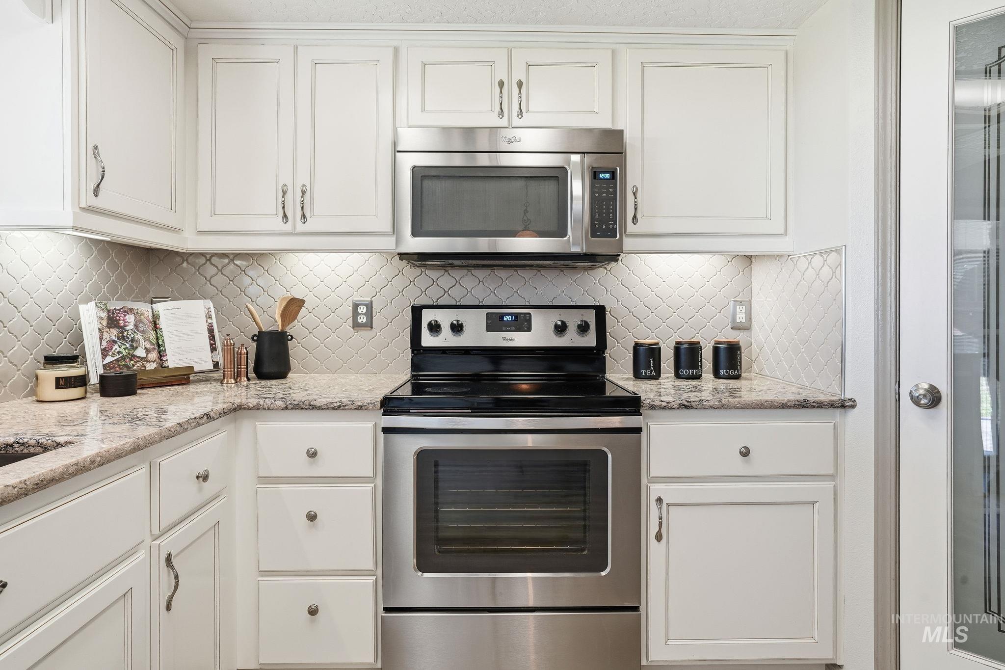 Kitchen with appliances with stainless steel finishes, white cabinetry, and light stone counters