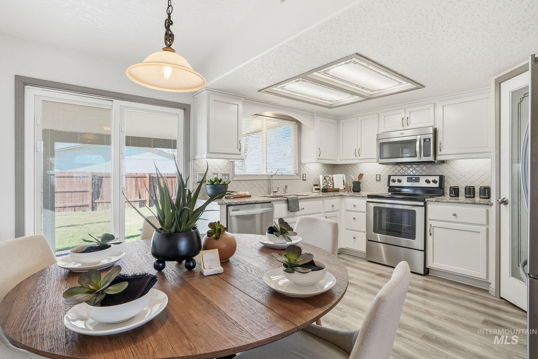 Kitchen featuring appliances with stainless steel finishes, white cabinetry, light stone countertops, a textured ceiling, and light wood-style floors