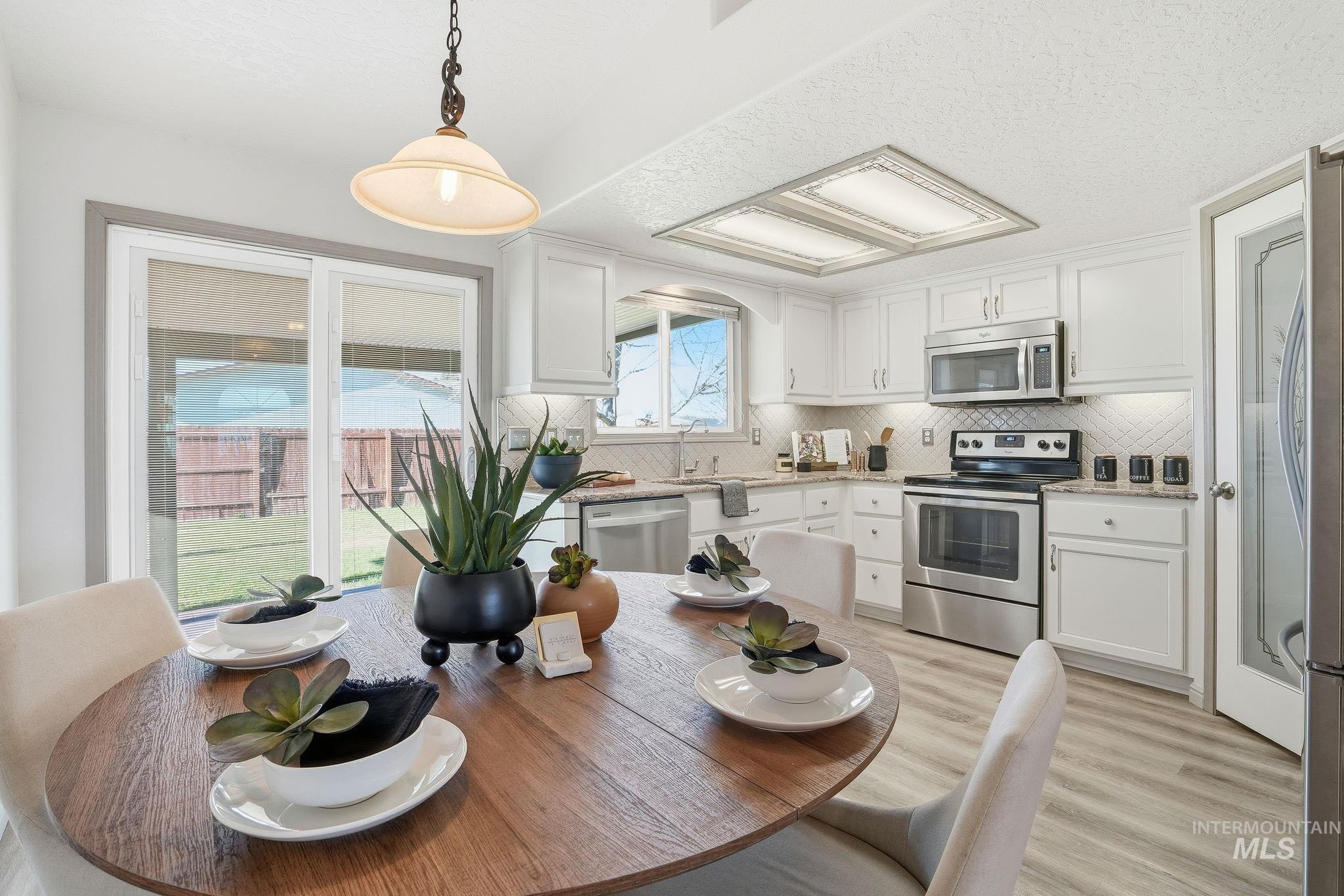 Kitchen with appliances with stainless steel finishes, white cabinets, a textured ceiling, hanging light fixtures, and light wood finished floors