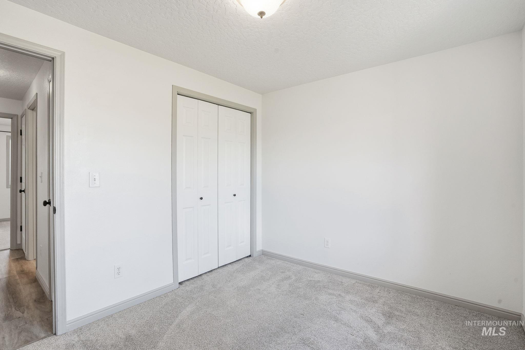 Unfurnished bedroom featuring a textured ceiling, light colored carpet, and a closet