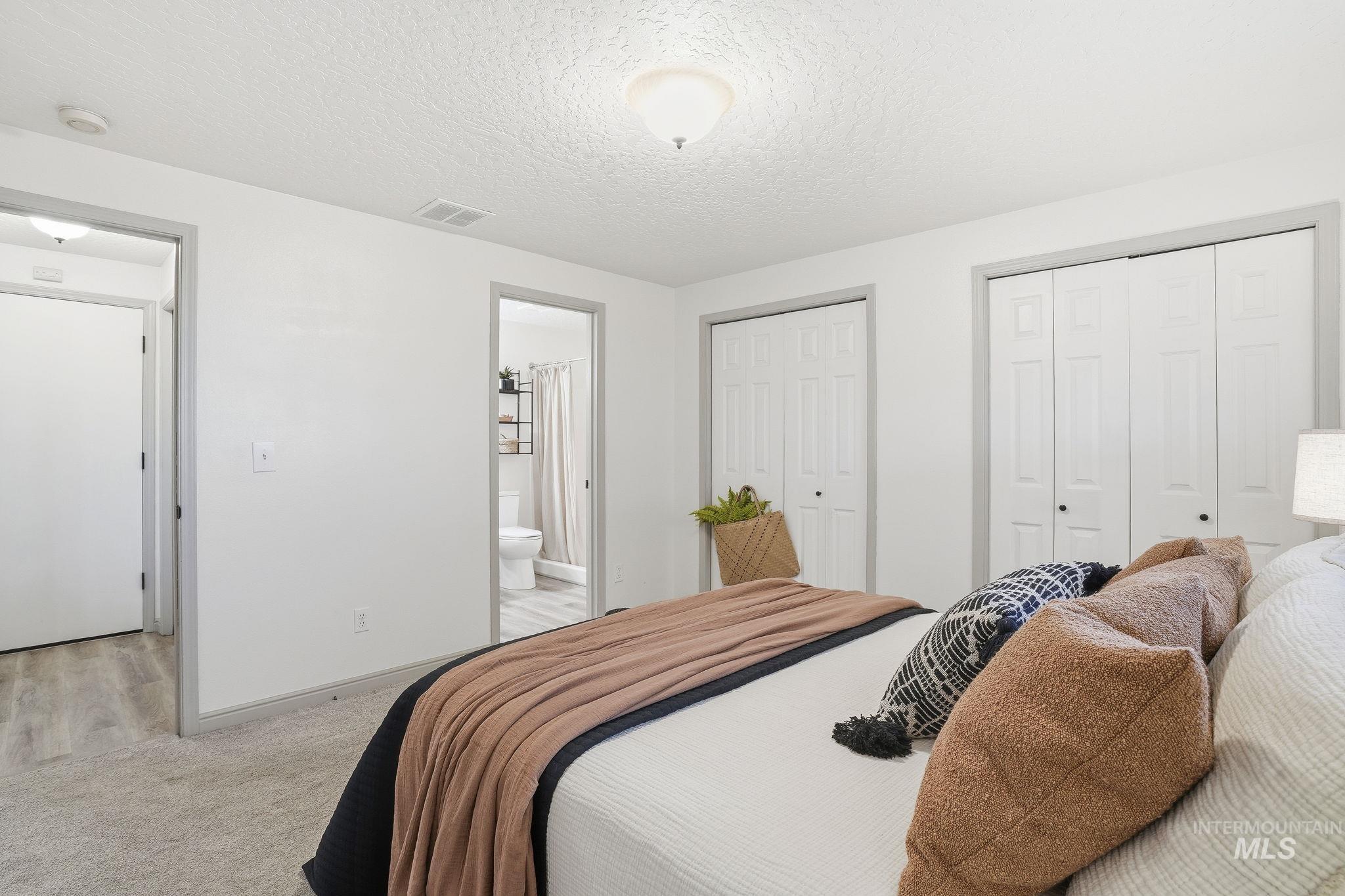 Carpeted bedroom featuring multiple closets, a textured ceiling, and connected bathroom