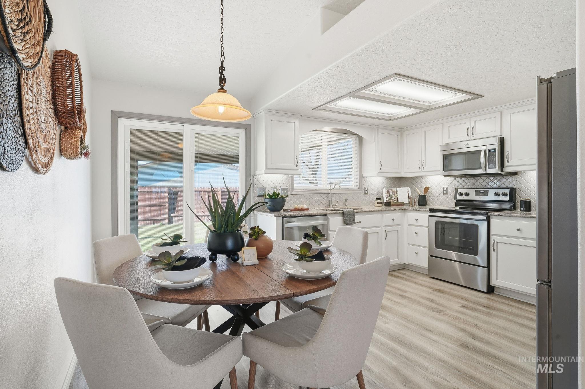 Kitchen featuring appliances with stainless steel finishes, a textured ceiling, white cabinetry, hanging light fixtures, and light wood-style floors