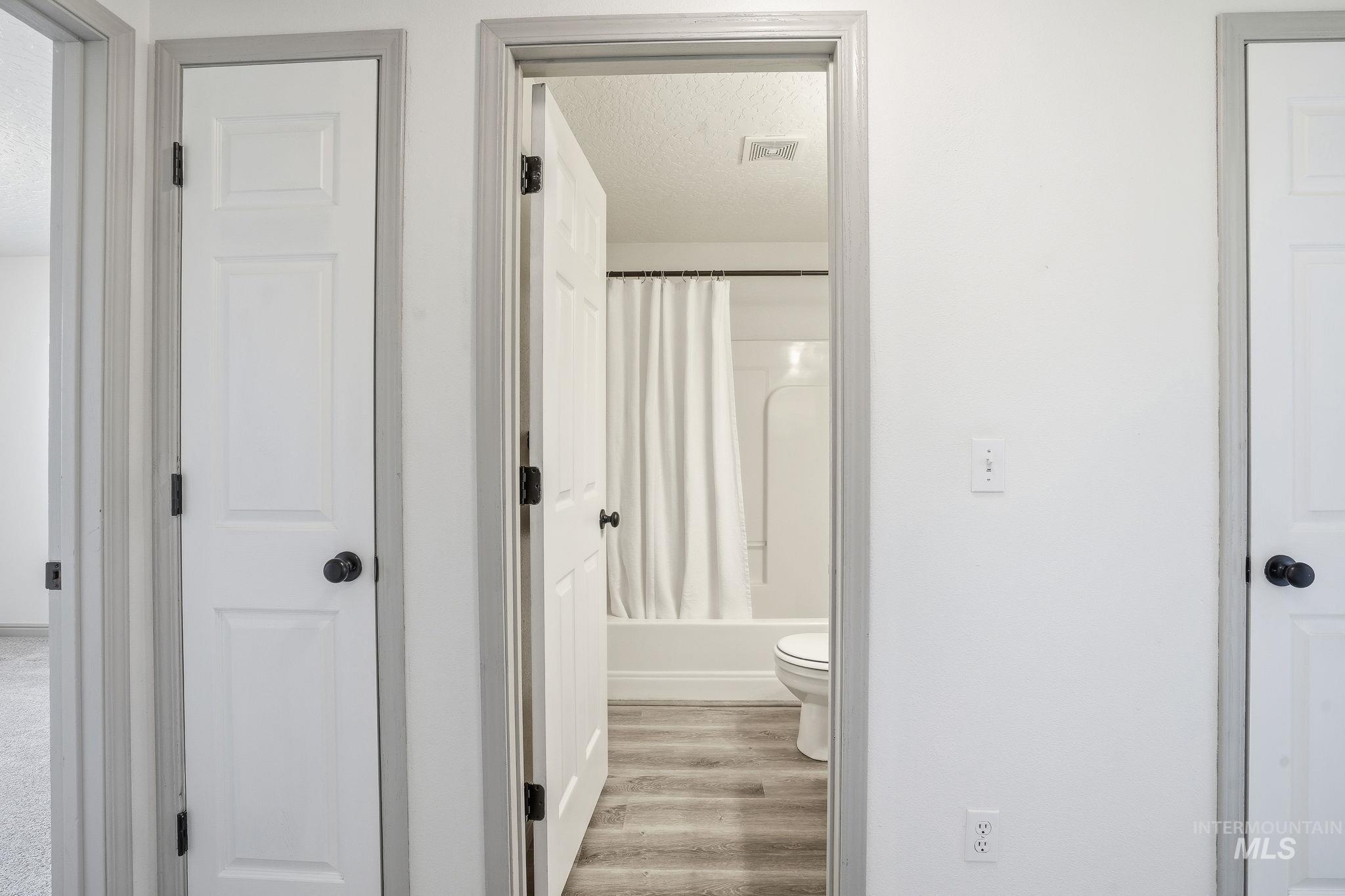 Full bath with light wood finished floors, shower / tub combo with curtain, and a textured ceiling