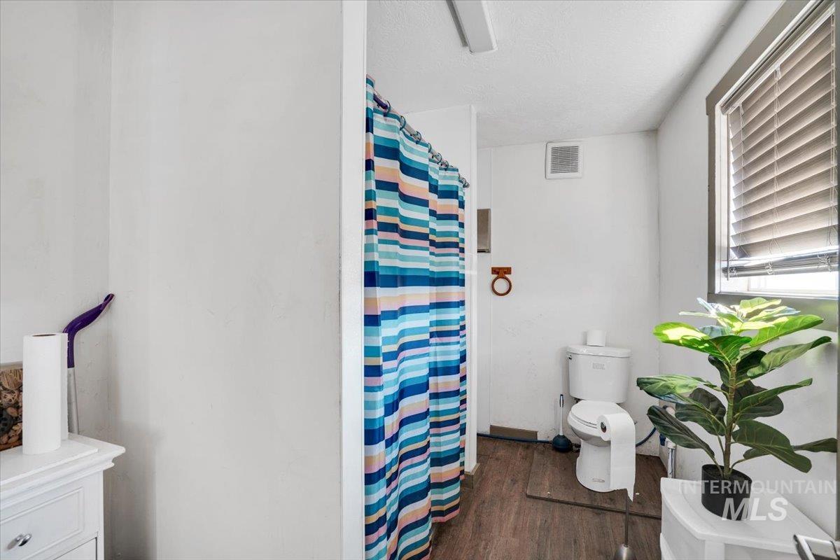 Full bathroom featuring curtained shower, dark wood-type flooring, and a textured ceiling