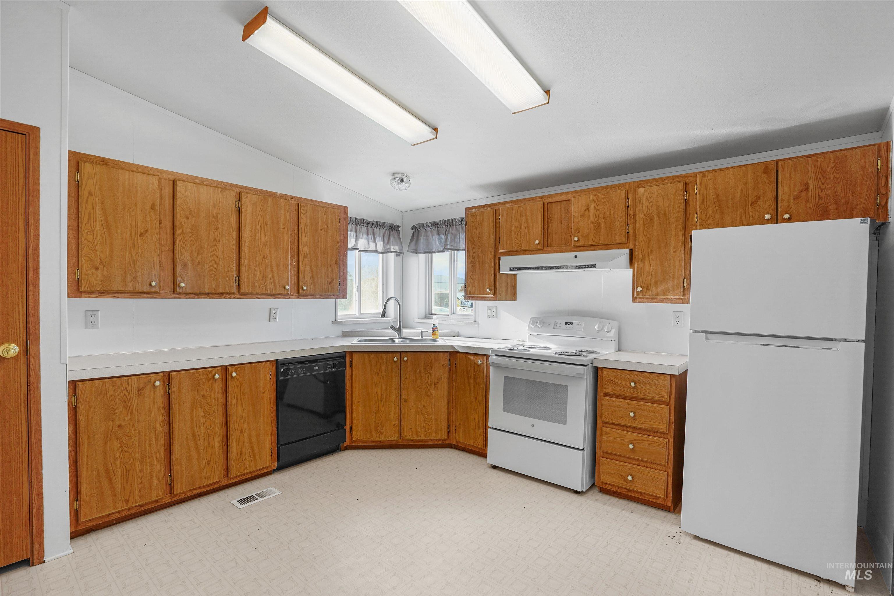 Kitchen featuring light flooring, vaulted ceiling, white appliances, light countertops, and brown cabinets