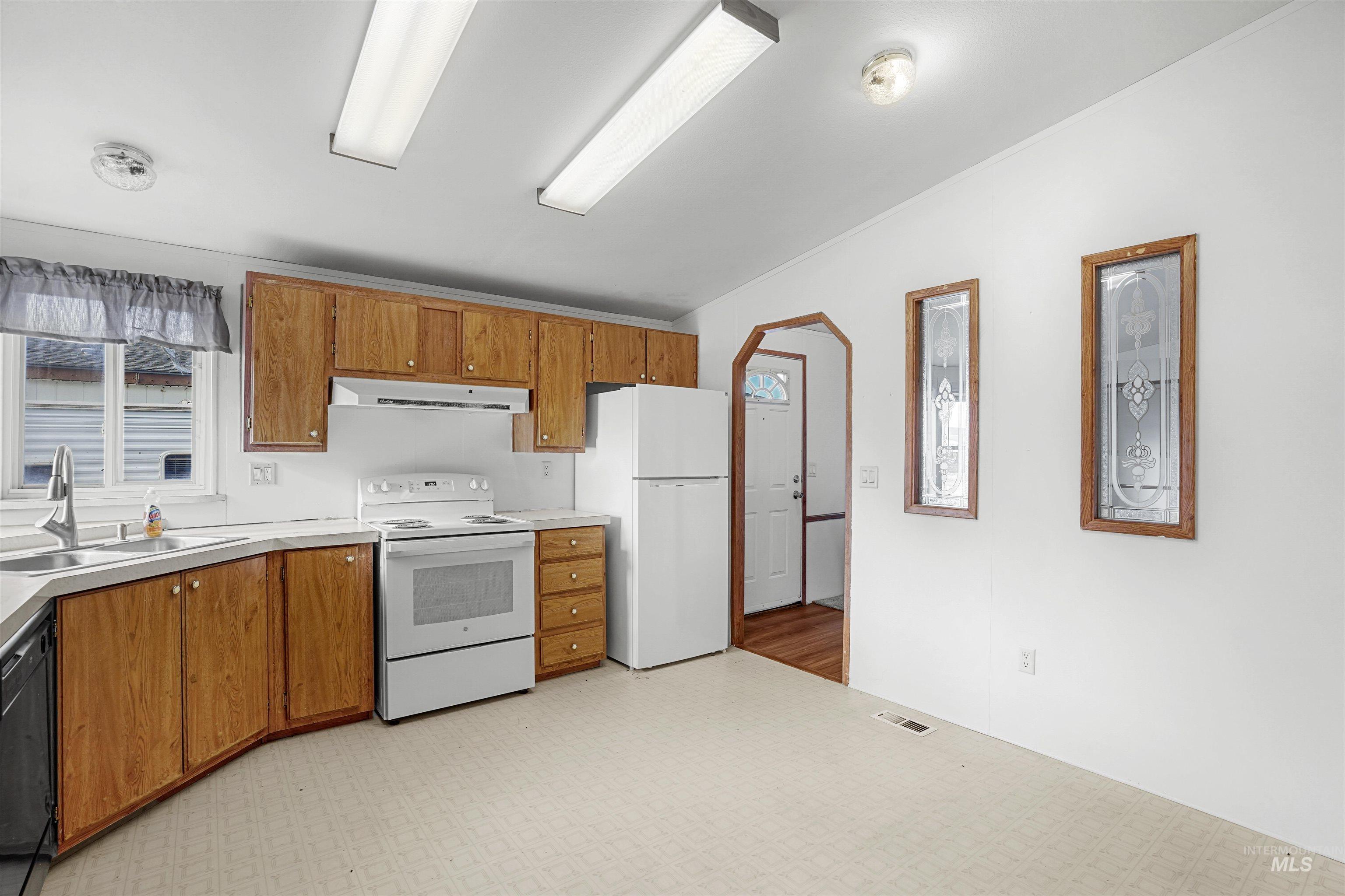 Kitchen featuring arched walkways, white appliances, light floors, brown cabinetry, and light countertops