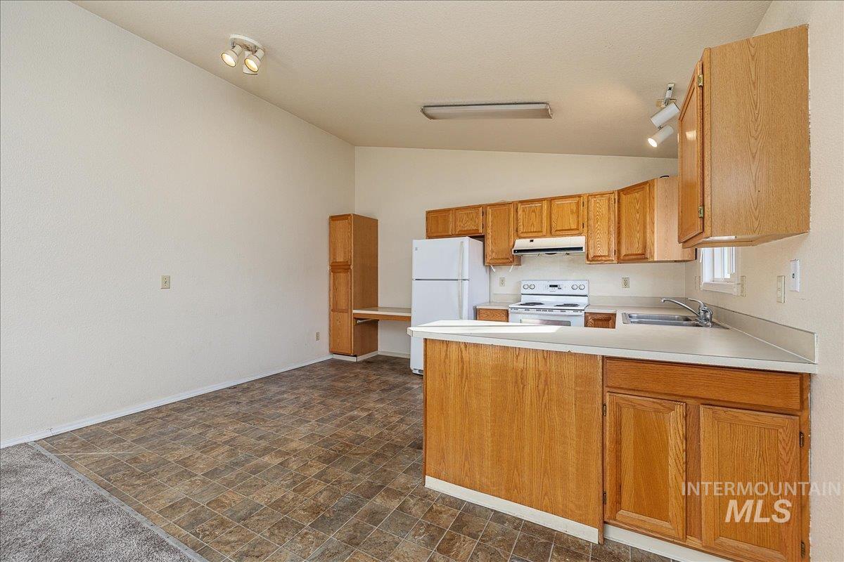 Kitchen with lofted ceiling, a peninsula, light countertops, white appliances, and under cabinet range hood