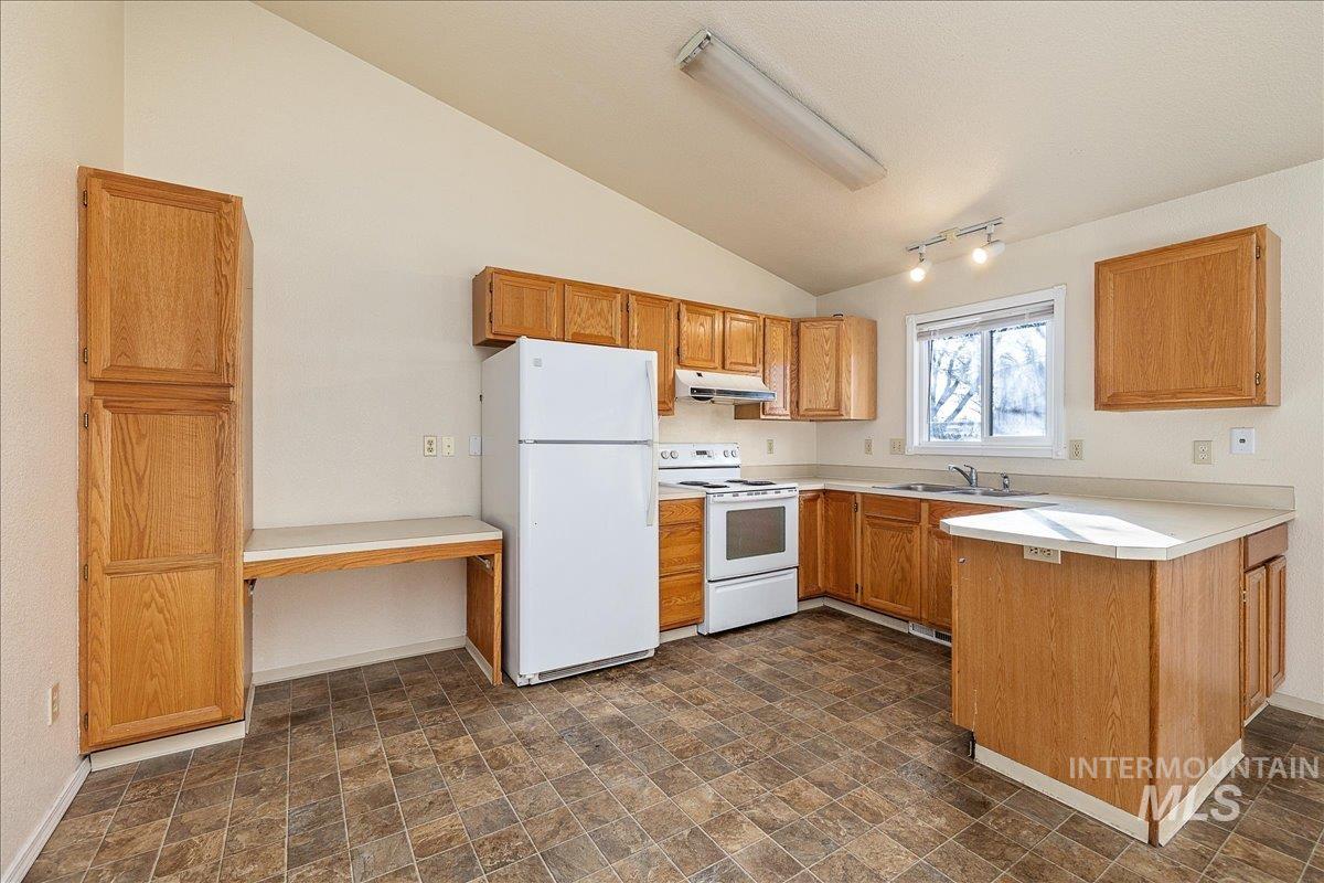 Kitchen featuring white appliances, light countertops, vaulted ceiling, a peninsula, and brown cabinetry