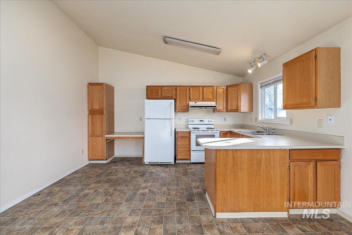 Kitchen featuring light countertops, white appliances, brown cabinetry, a peninsula, and lofted ceiling