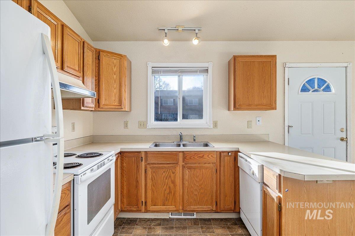 Kitchen with white appliances, light countertops, brown cabinetry, under cabinet range hood, and a peninsula