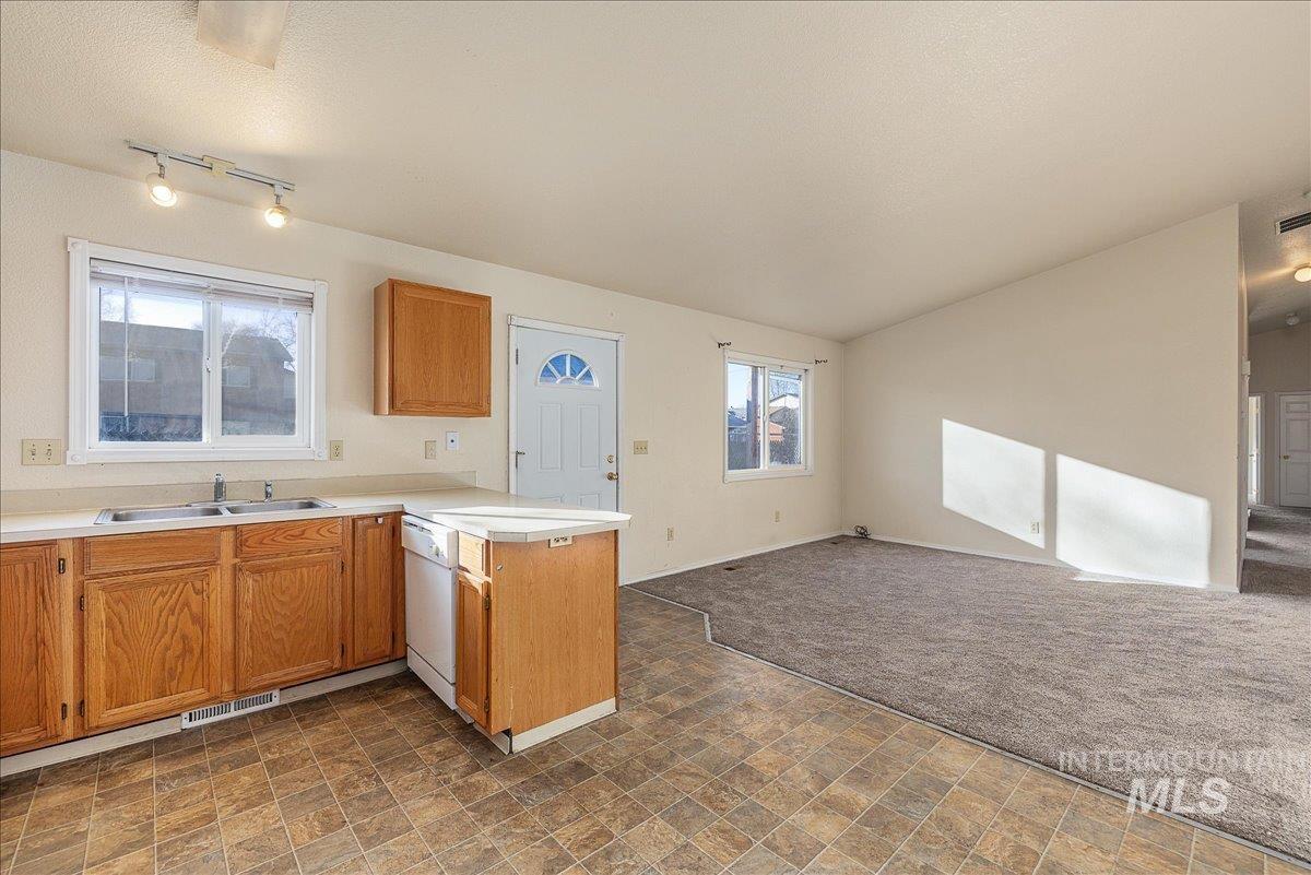 Kitchen featuring a peninsula, open floor plan, light countertops, dishwasher, and brown cabinetry
