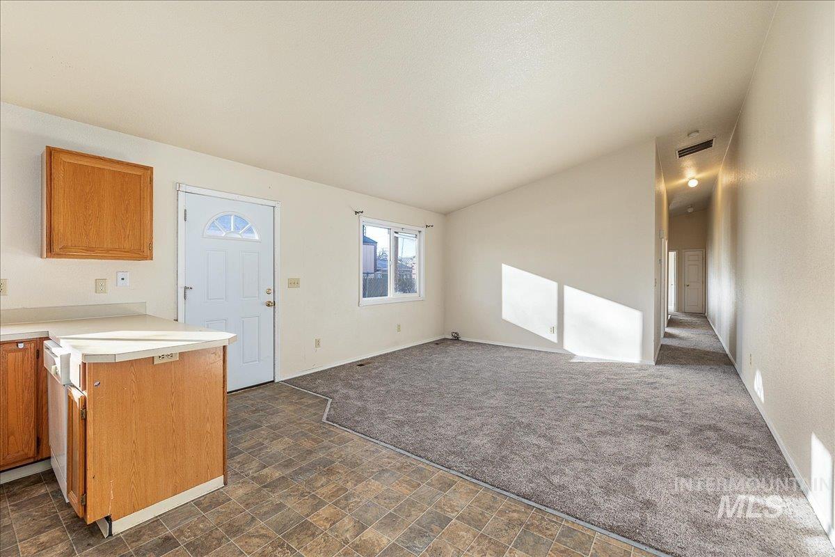 Kitchen featuring light countertops, brown cabinets, dark carpet, vaulted ceiling, and open floor plan