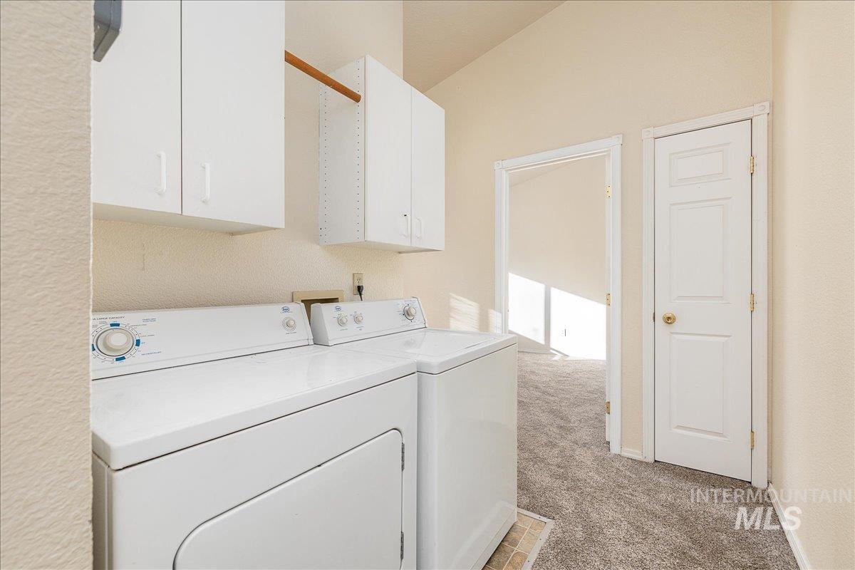 Laundry area featuring light carpet, cabinet space, washer and clothes dryer, and lofted ceiling