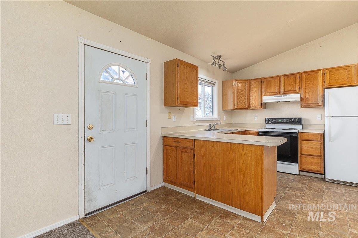 Kitchen featuring electric range oven, freestanding refrigerator, light countertops, brown cabinets, and lofted ceiling
