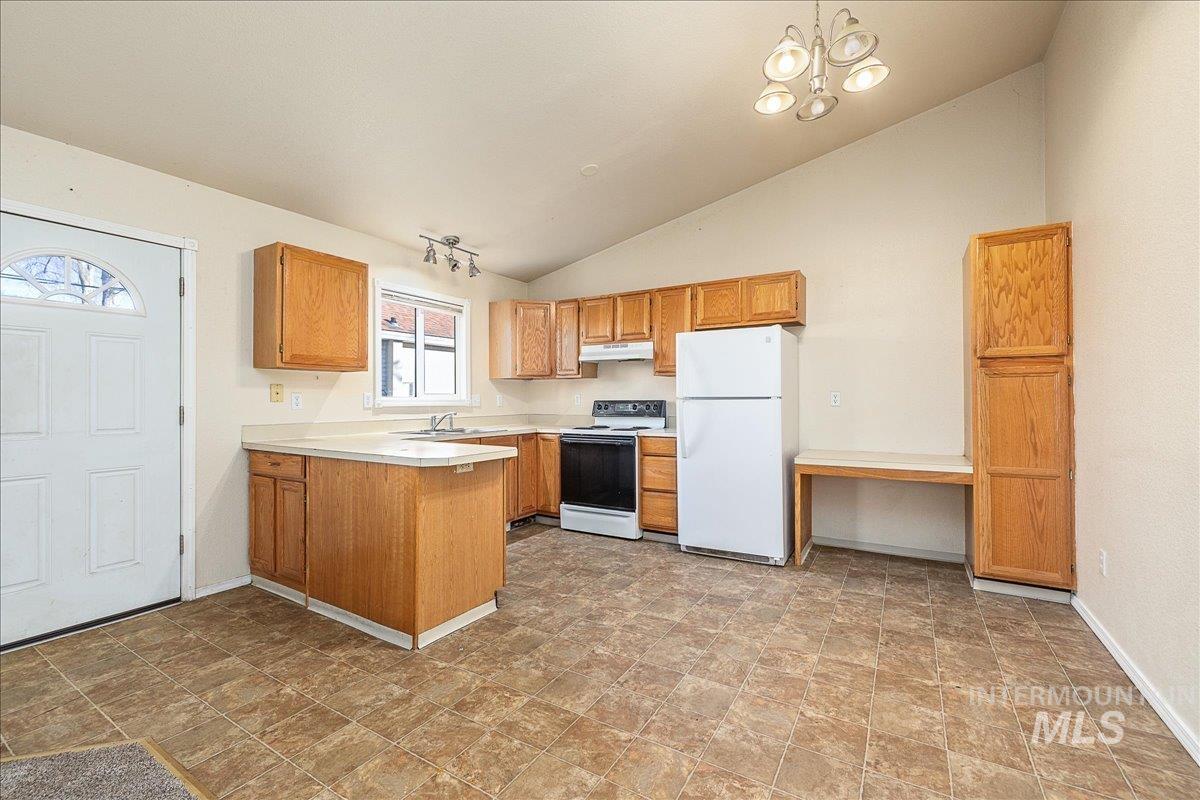 Kitchen featuring light countertops, white appliances, vaulted ceiling, a peninsula, and a chandelier