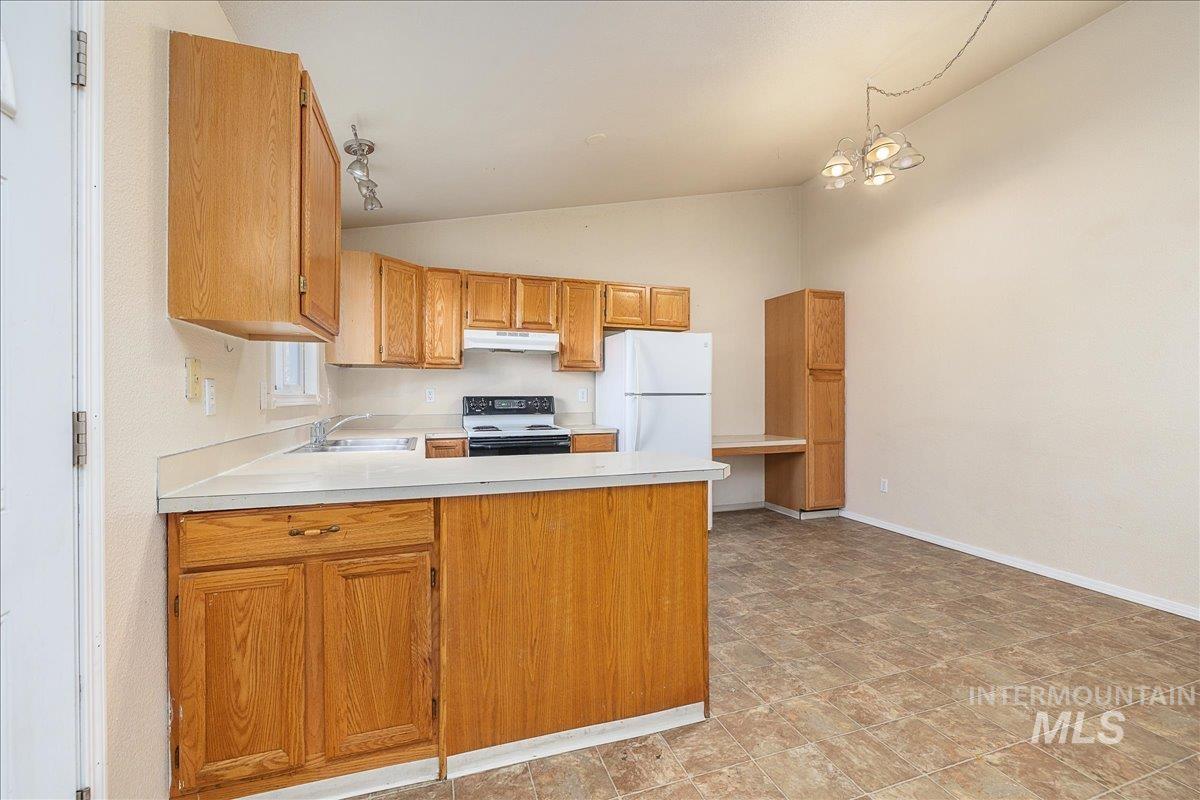 Kitchen with light countertops, a peninsula, range with electric stovetop, freestanding refrigerator, and brown cabinets