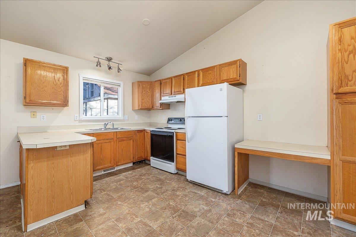 Kitchen with light countertops, white appliances, lofted ceiling, brown cabinets, and stone finish flooring