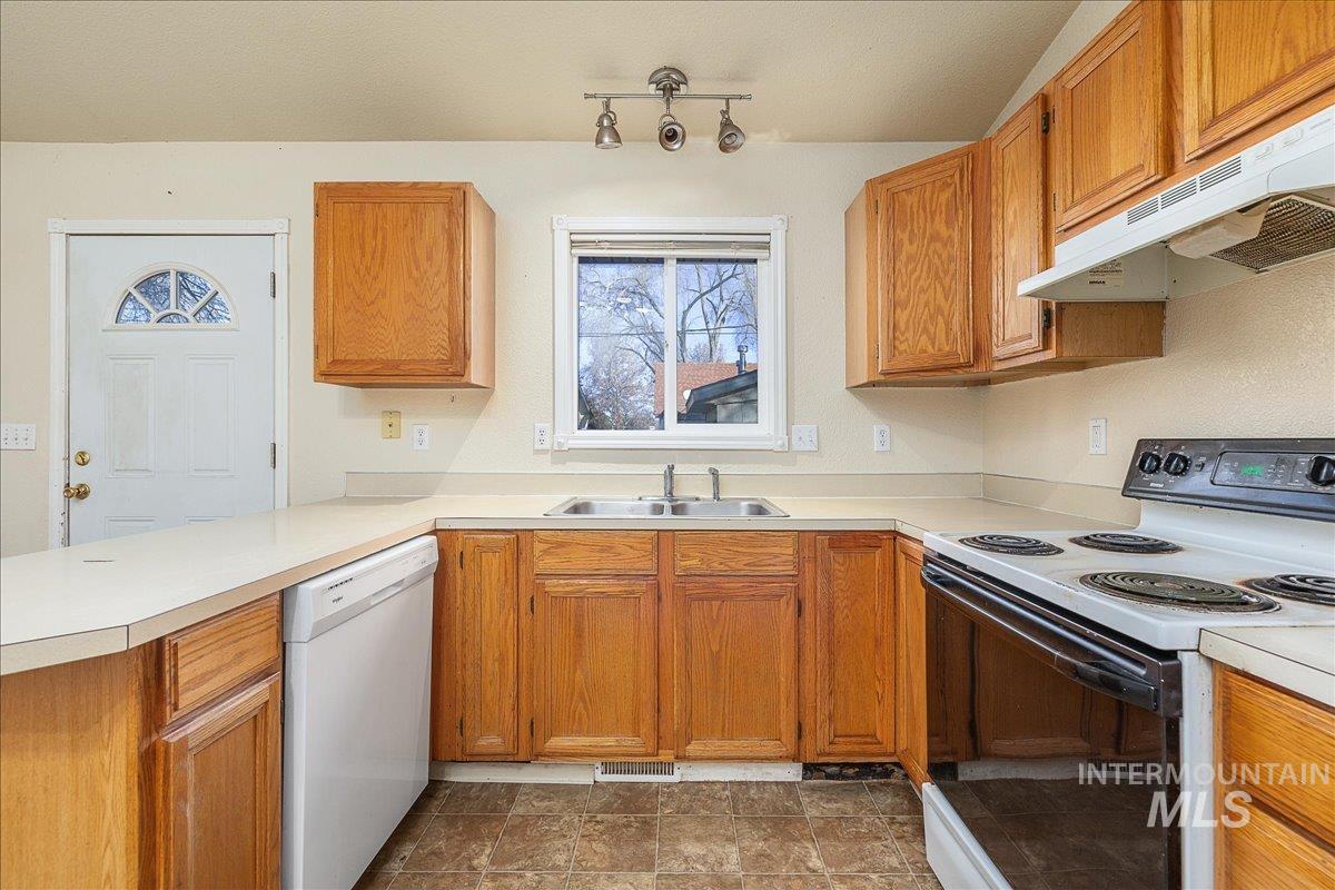 Kitchen featuring electric stove, brown cabinetry, white dishwasher, and light countertops