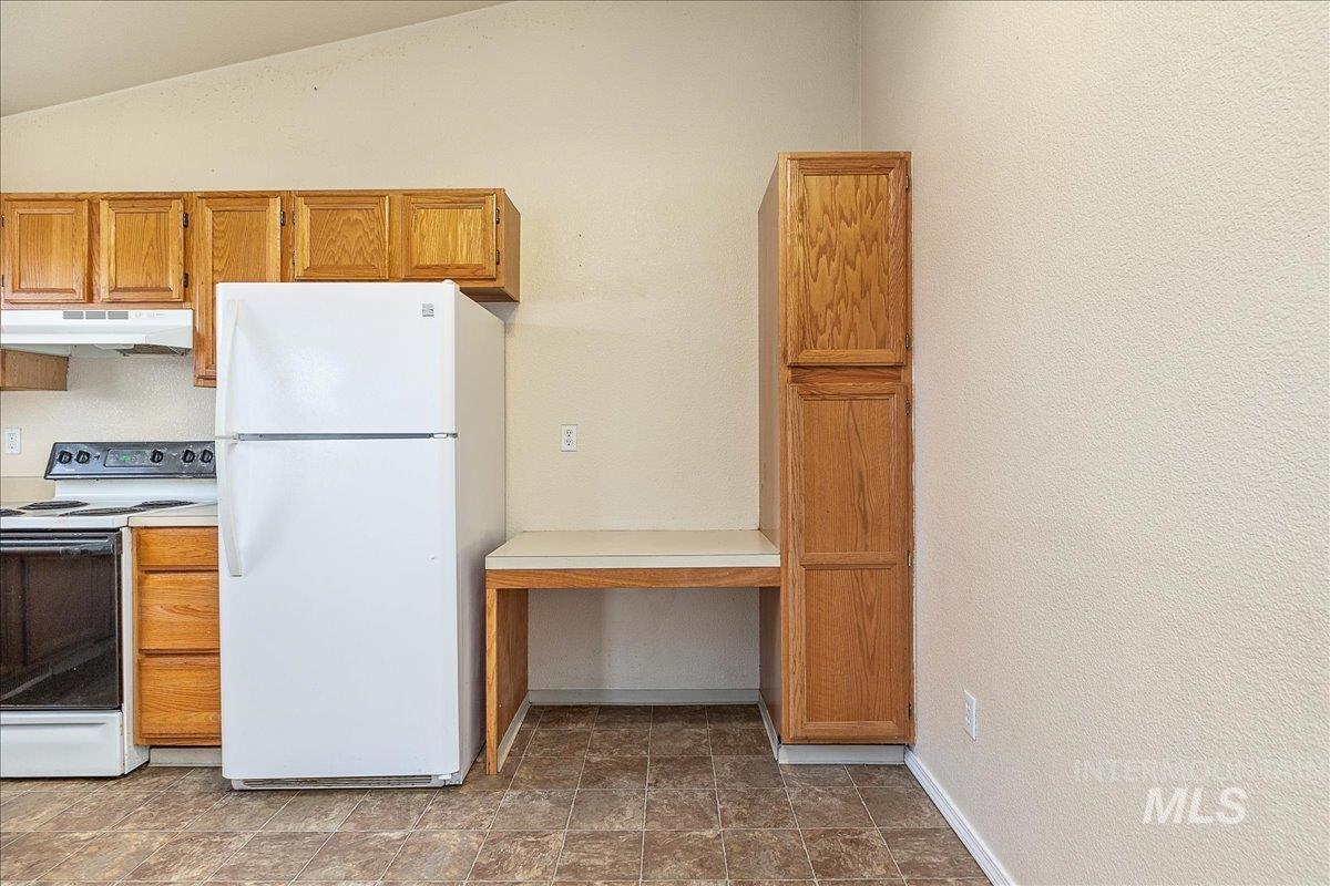 Kitchen featuring white appliances, brown cabinets, light countertops, under cabinet range hood, and vaulted ceiling