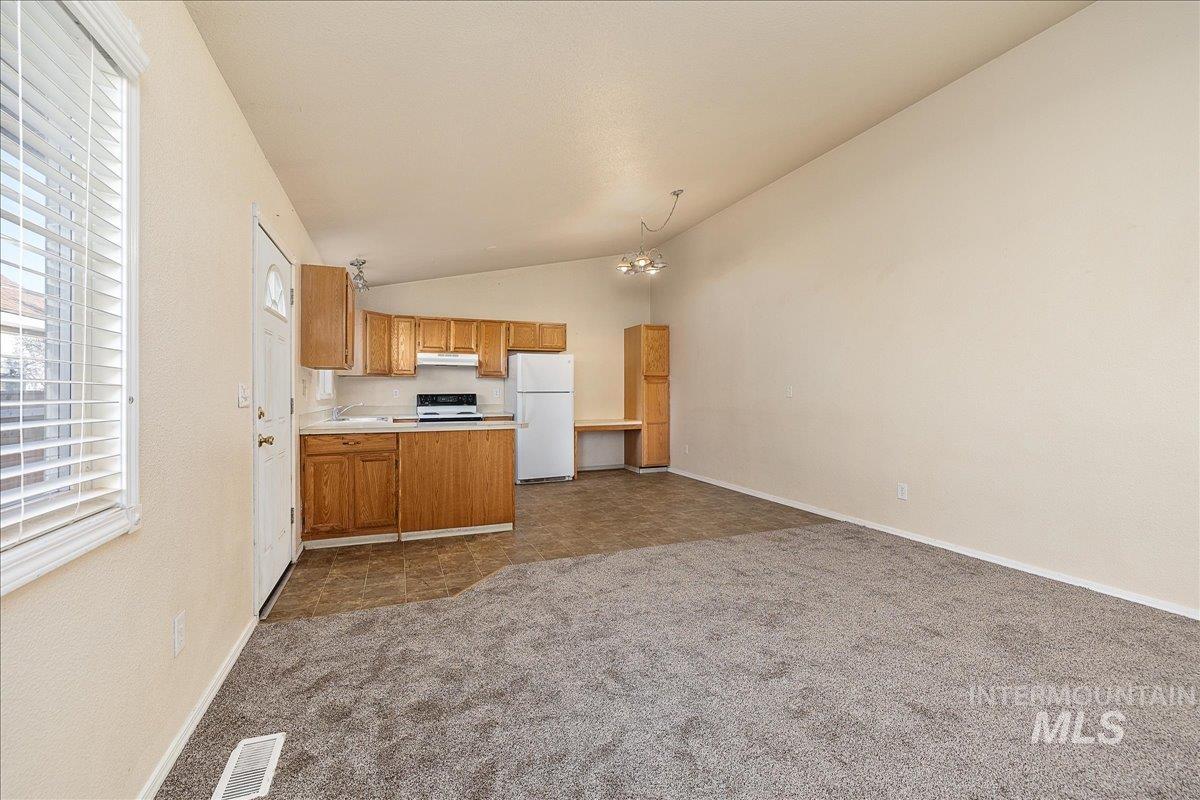 Kitchen with open floor plan, light countertops, lofted ceiling, freestanding refrigerator, and dark colored carpet