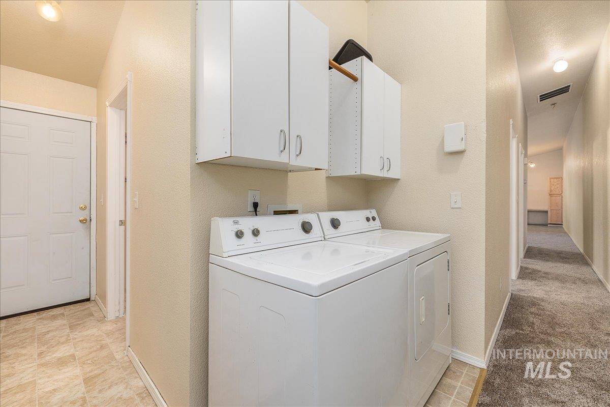 Washroom with a textured wall, washer and clothes dryer, and cabinet space