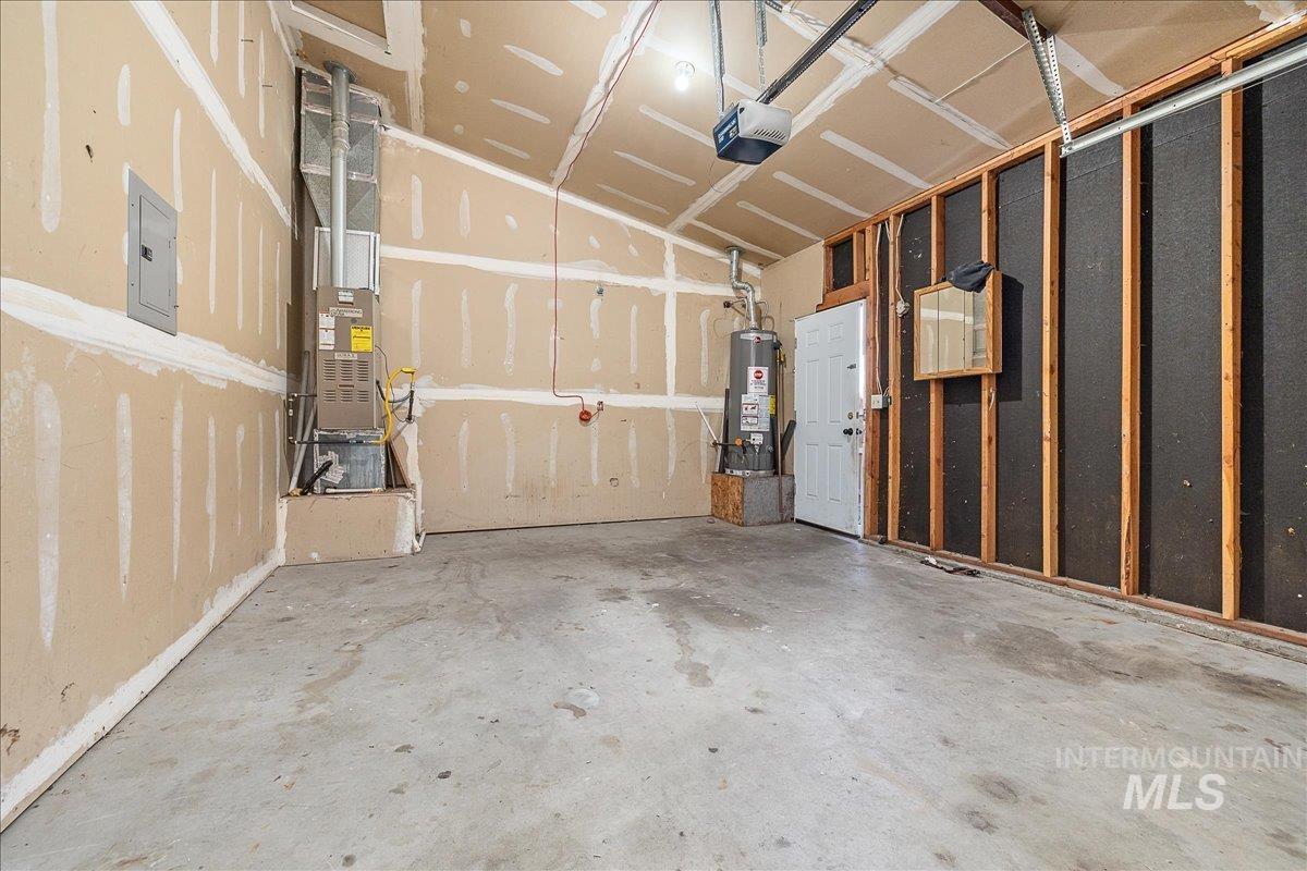 Garage featuring electric panel, gas water heater, a garage door opener, and heating unit