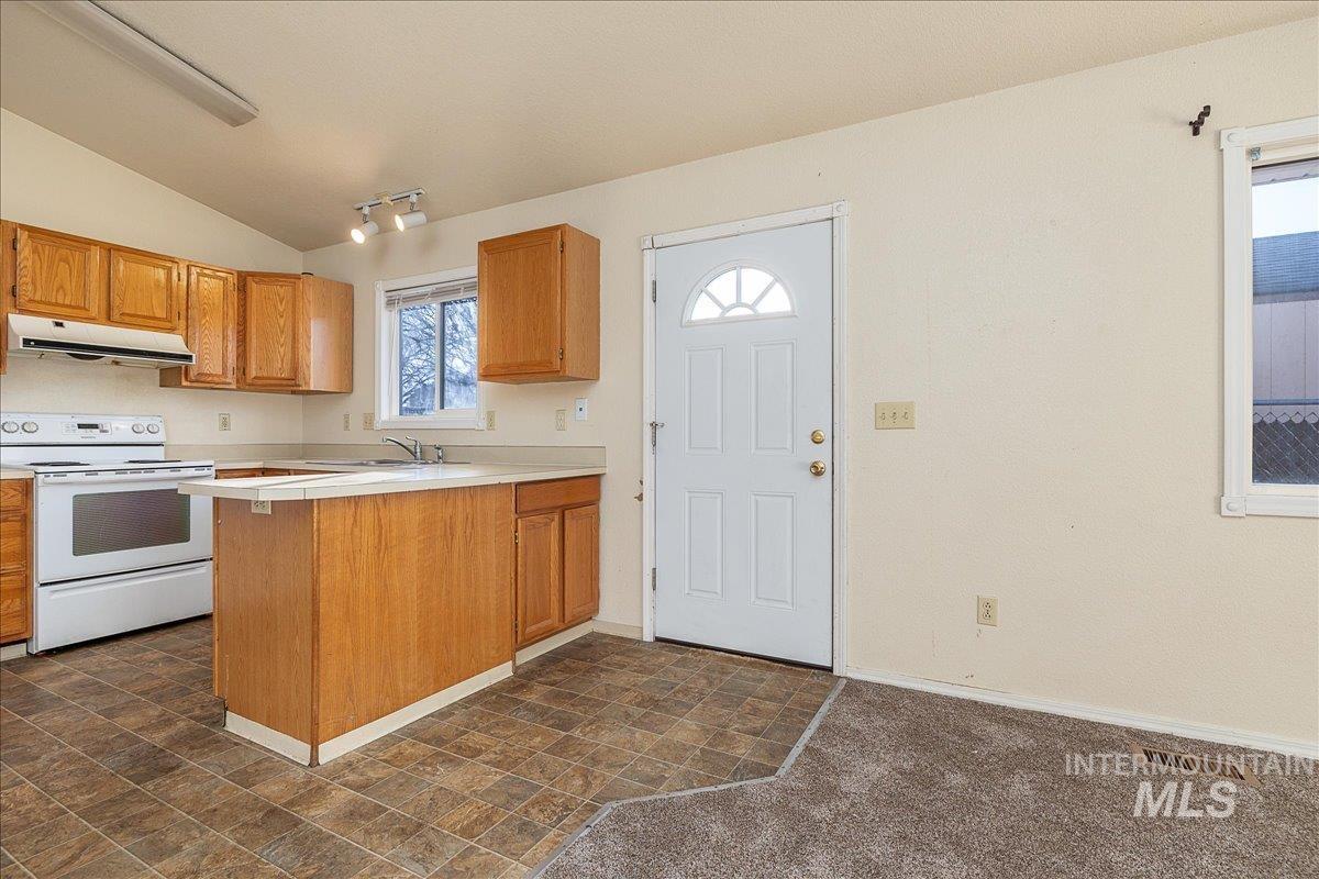 Kitchen with white electric range oven, a peninsula, under cabinet range hood, lofted ceiling, and brown cabinets