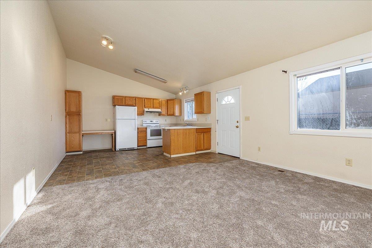 Kitchen featuring light countertops, open floor plan, lofted ceiling, white appliances, and brown cabinetry