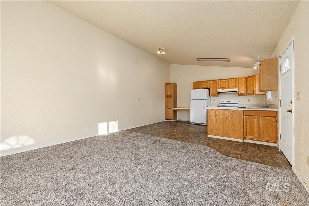 Kitchen featuring lofted ceiling, open floor plan, dark carpet, light countertops, and white appliances