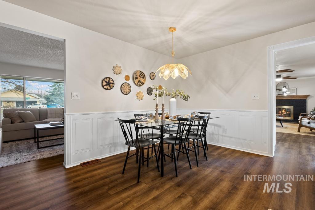 Dining room featuring a decorative wall, a wainscoted wall, a brick fireplace, and dark wood finished floors