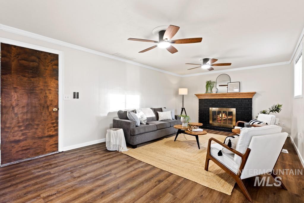 Living area with a fireplace, dark wood-style floors, ornamental molding, and a ceiling fan