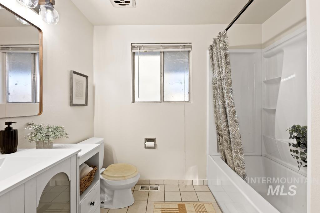 Bathroom with shower / tub combo with curtain, light tile patterned floors, and vanity