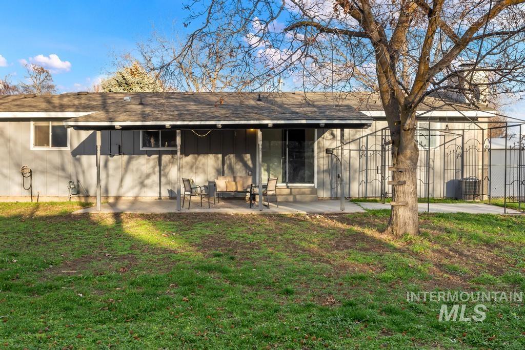 Back of property with board and batten siding, a shingled roof, a patio, and a yard
