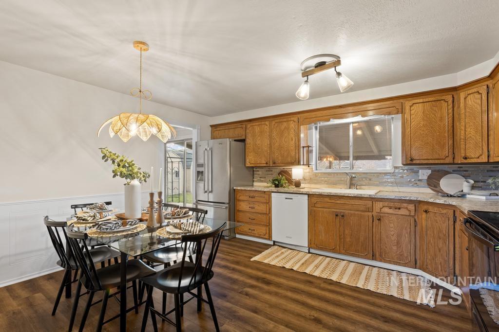 Kitchen featuring brown cabinets, pendant lighting, high end refrigerator, dishwasher, and dark wood-style floors