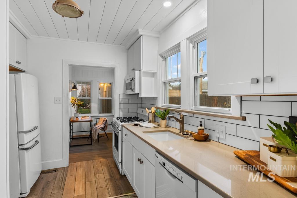 Kitchen featuring white appliances, tasteful backsplash, dark wood-style floors, white cabinets, and crown molding