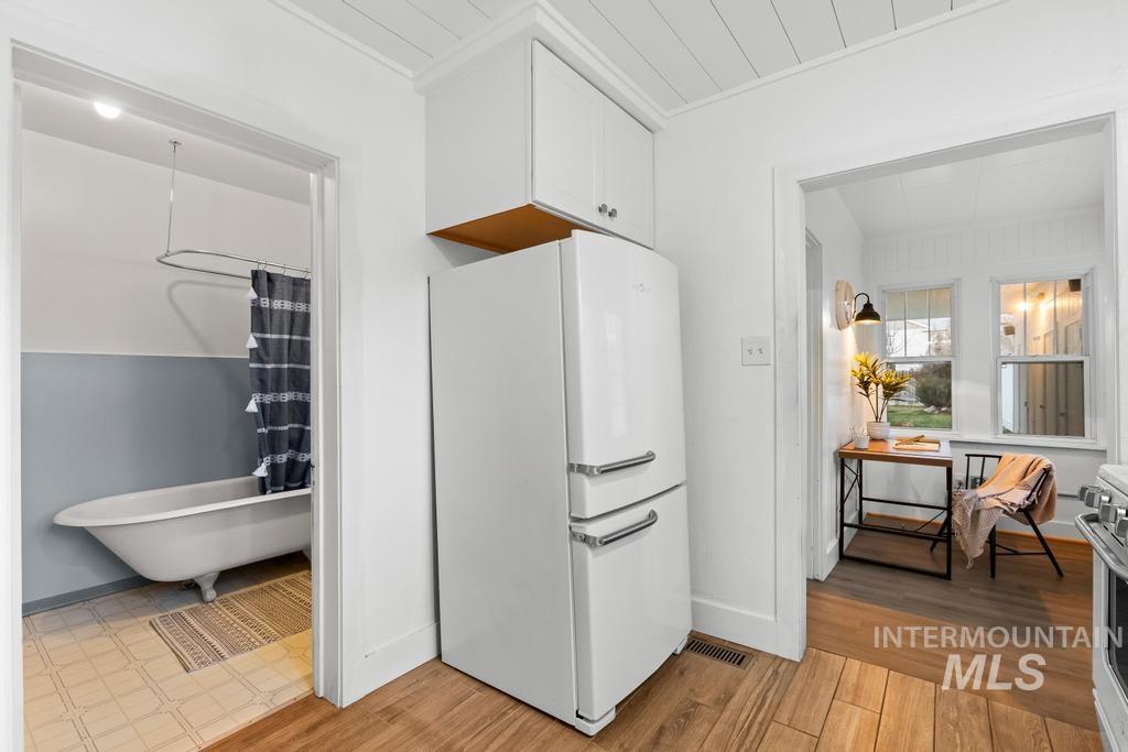 Kitchen with freestanding refrigerator, white cabinetry, light wood finished floors, and stainless steel range oven