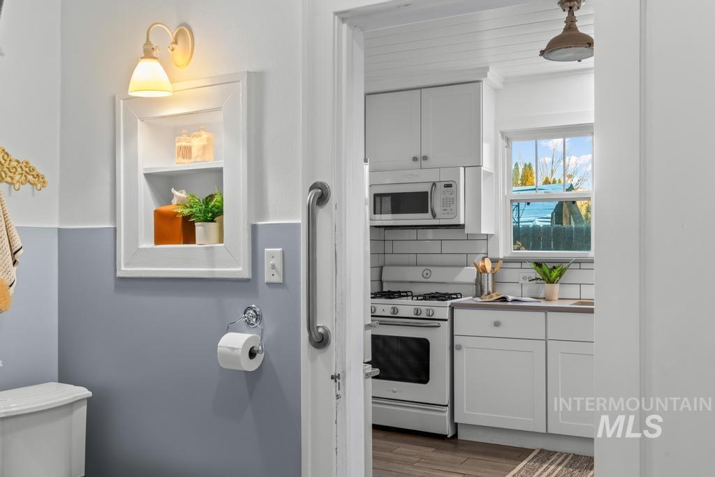 Kitchen with white cabinets, white appliances, decorative backsplash, light wood-type flooring, and light countertops