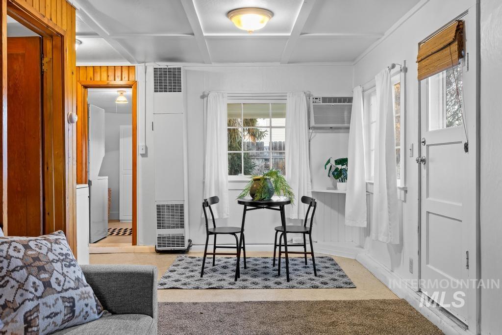 Sitting room with a heating unit, coffered ceiling, wood walls, light colored carpet, and a wall mounted AC