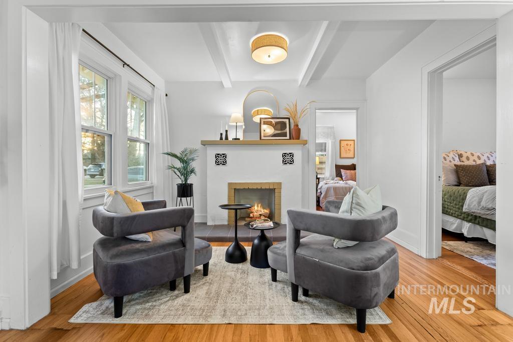 Living area with beam ceiling, a lit fireplace, and light wood-type flooring
