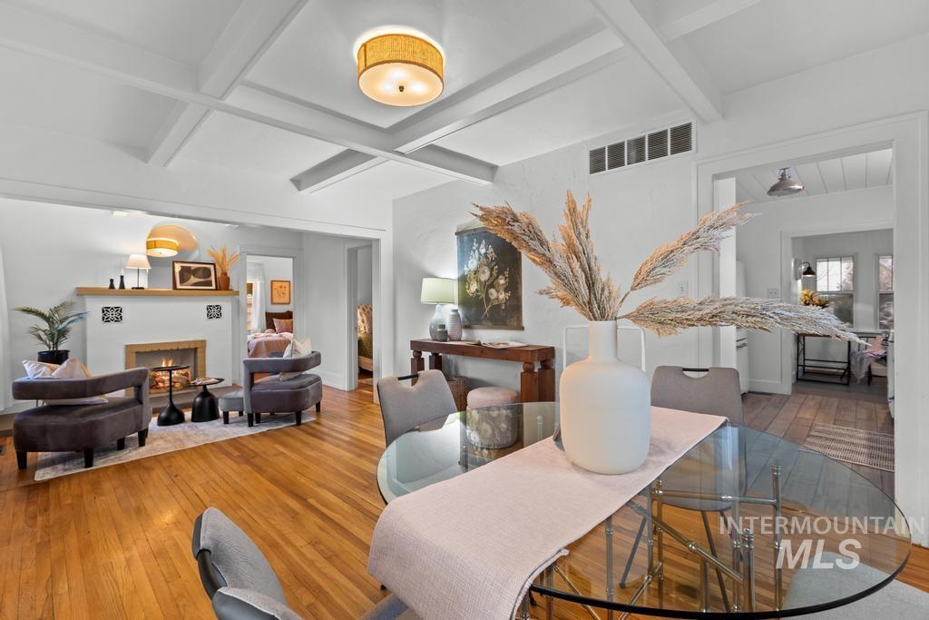 Dining space with beamed ceiling, hardwood / wood-style floors, coffered ceiling, and a lit fireplace