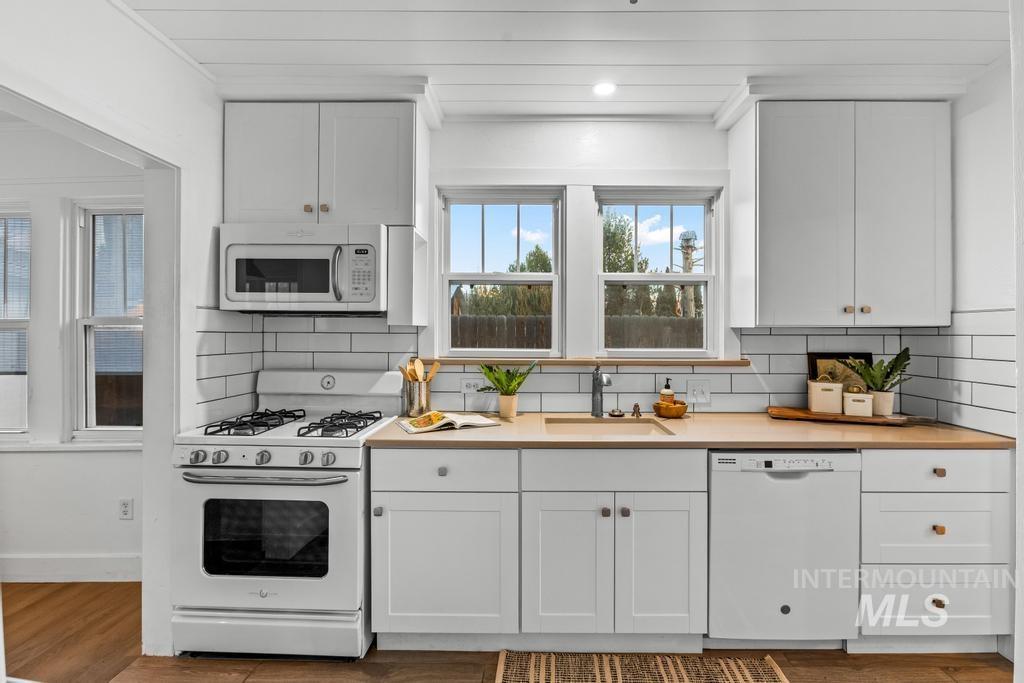Kitchen with white appliances, backsplash, white cabinetry, and light wood finished floors