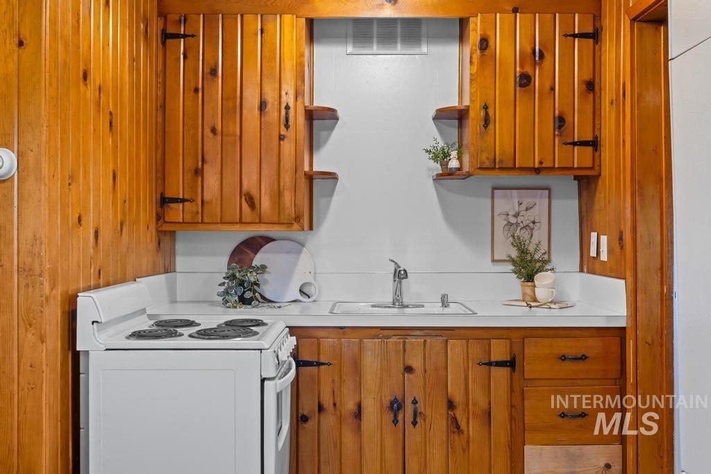 Kitchen with white electric range, light countertops, open shelves, brown cabinetry, and wooden walls