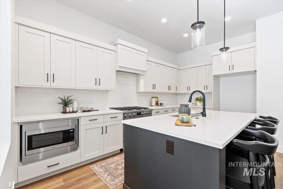 Kitchen featuring decorative backsplash, an island with sink, stainless steel appliances, decorative light fixtures, and recessed lighting