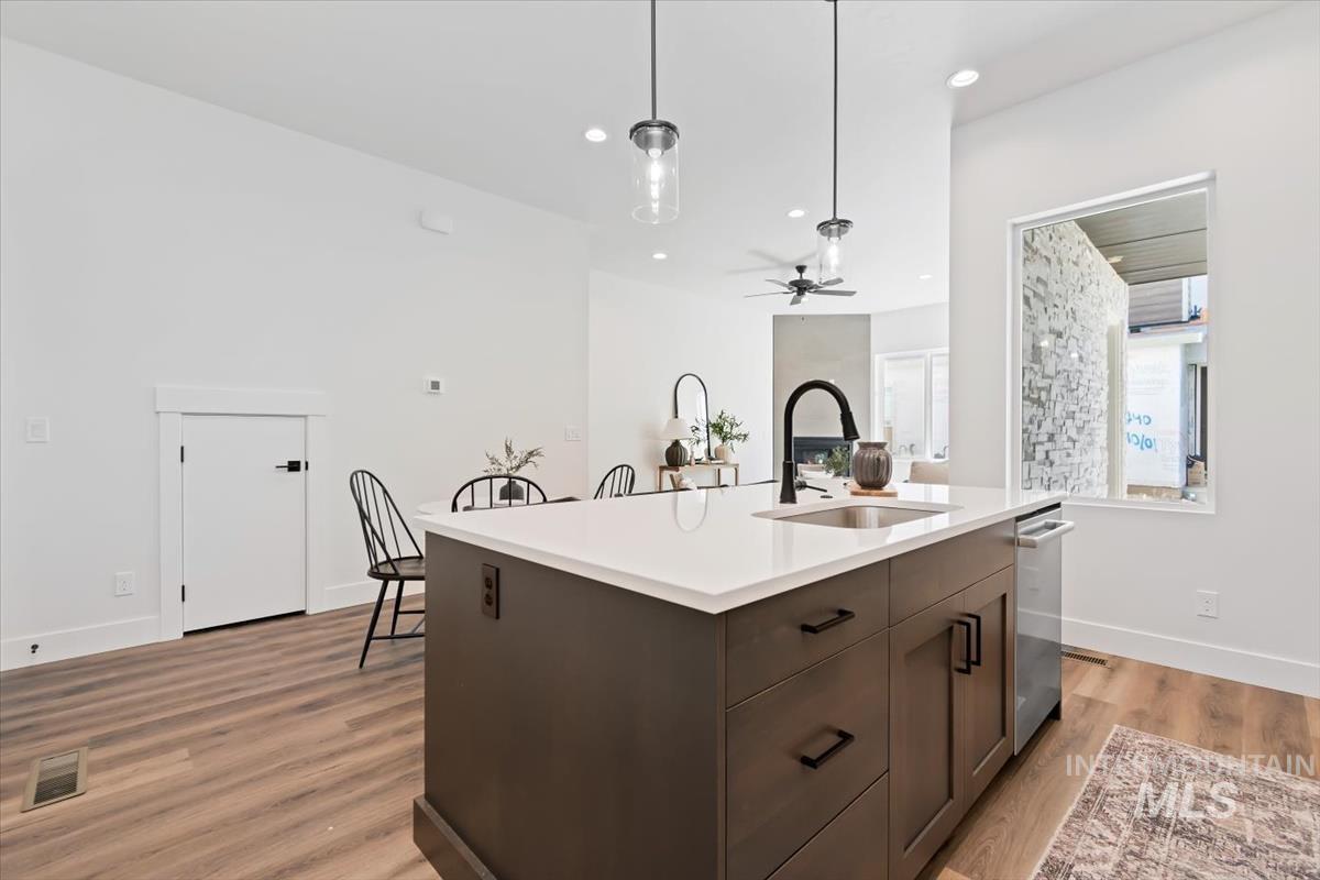 Kitchen featuring dark brown cabinetry, decorative light fixtures, light wood-style floors, a kitchen island with sink, and recessed lighting