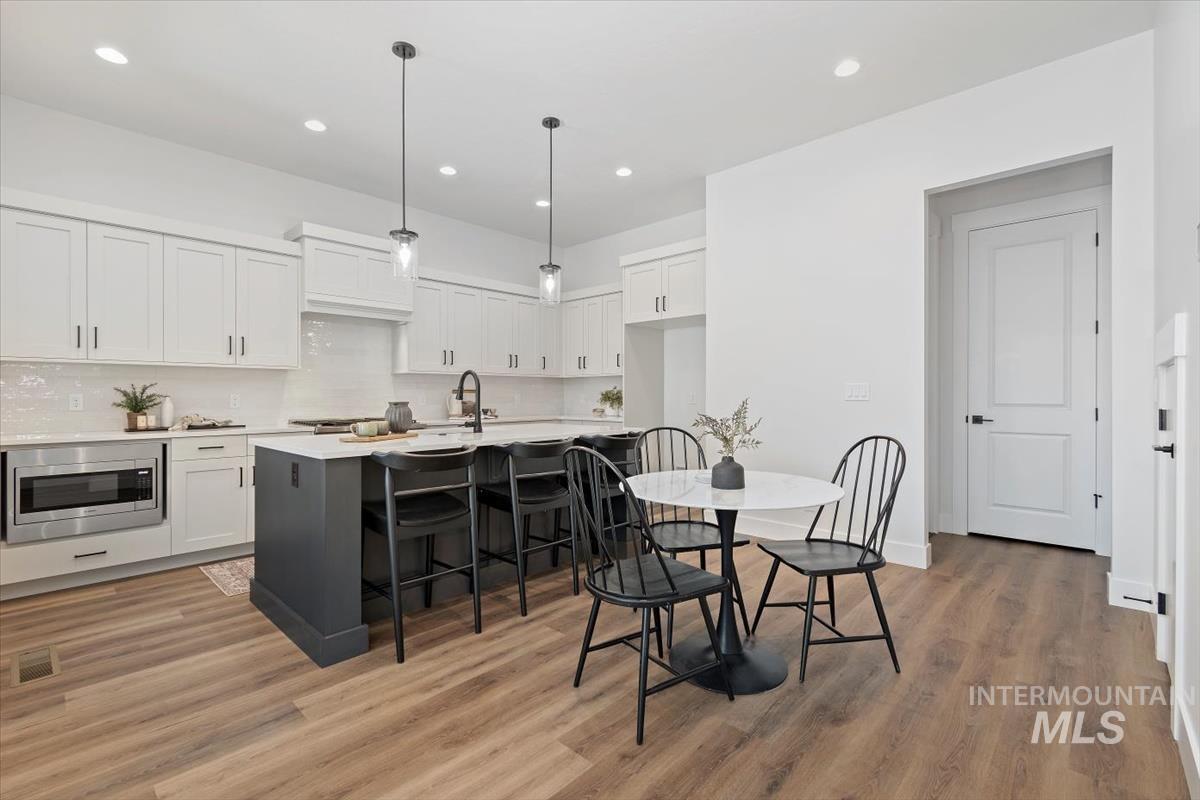 Kitchen featuring pendant lighting, a breakfast bar, white cabinets, an island with sink, and recessed lighting