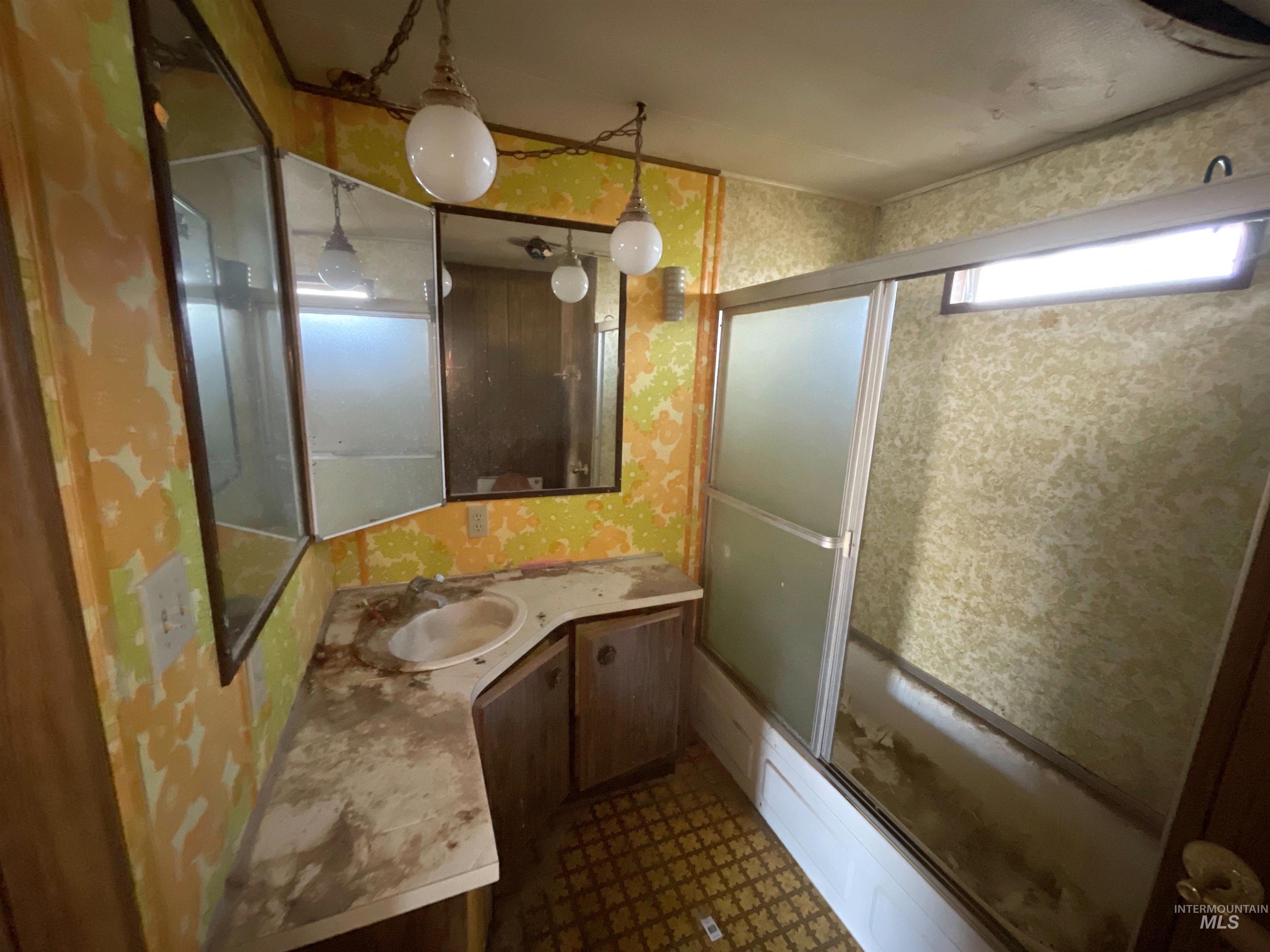 Full bathroom featuring wallpapered walls, shower / bath combination with glass door, and vanity