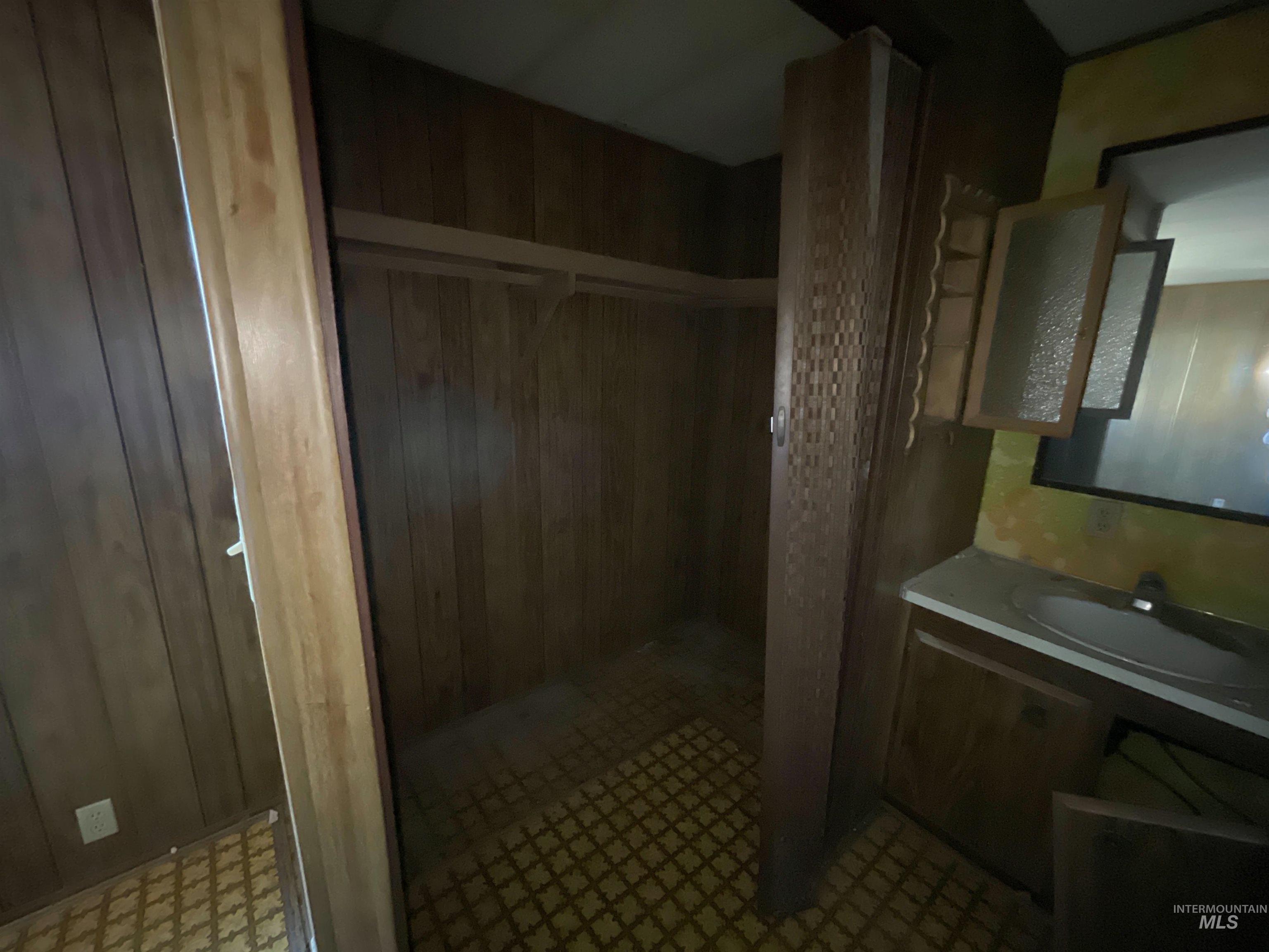 Full bath with vanity, wood walls, tiled shower, and light flooring