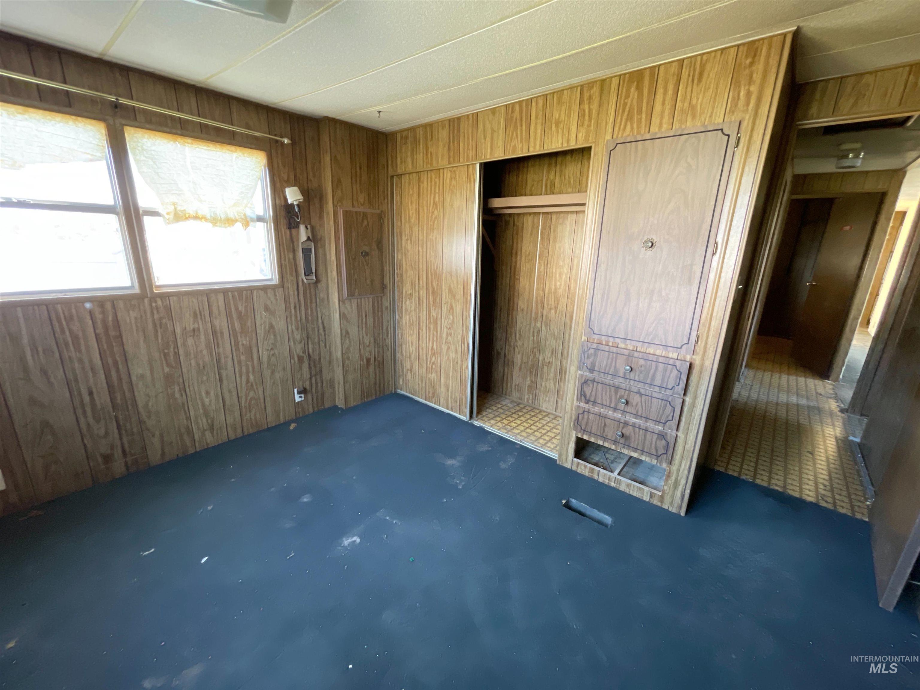 Unfurnished bedroom with wooden walls, carpet, and a closet